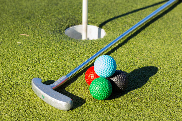 A closeup shot of four colorful golf balls next to the golf club close to the goal hole - Φωτογραφία, εικόνα