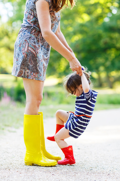 Mother and little adorable child girl in rubber boots having fun - Photo, Image