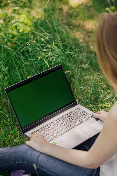 Dziewczyna siedzi na trawie i pracuje w laptopie. Wolny strzelec. samokształcenie. koncepcja kształcenia na odległość na zewnątrz - Zdjęcie, obraz