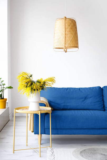 Jarrón con flores de mimosa en la mesa y sofá azul en la sala de estar ligera - Foto, Imagen