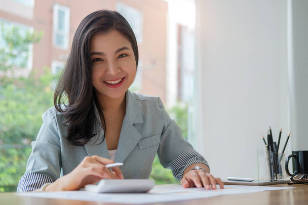 Молодая азиатская деловая женщина, сидящая на работе и читающая финансовый документ. - Фото, изображение