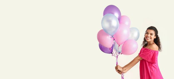 Portrait of happy African-American woman with balloons on light background with space for text - Fotoğraf, Görsel