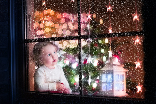 Carino ragazza bambino riccio seduto con un orso giocattolo a casa durante il periodo di Natale, preparandosi a festeggiare la vigilia di Natale
 - Foto, immagini
