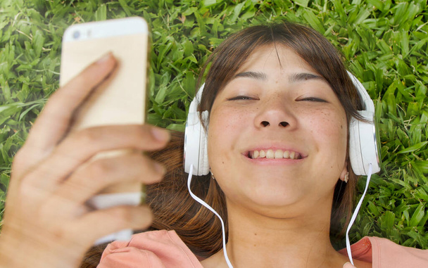 Heureuse adolescente asiatique allongée sur l'herbe entendre de la musique. Concept de légèreté - Photo, image