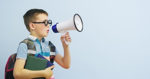 Little schoolboy with megaphone on blue background. Boy with megaphone making an announcement with copy space - Metraje, vídeo