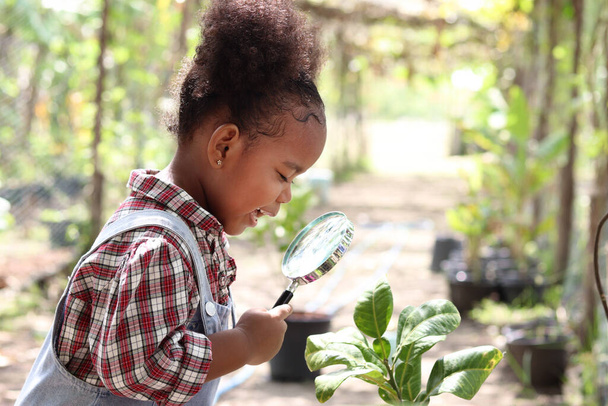 Szczęśliwa afrykańska dziewczyna z czarnymi kręconymi włosami trzyma lupę do zwiedzania formy ogrodu, dziecko obserwuje naturę z okularami powiększającymi, edukacja dzieci natury i planu - Zdjęcie, obraz