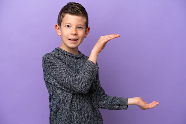 Little boy isolated on purple background holding copyspace to insert an ad - Foto, imagen