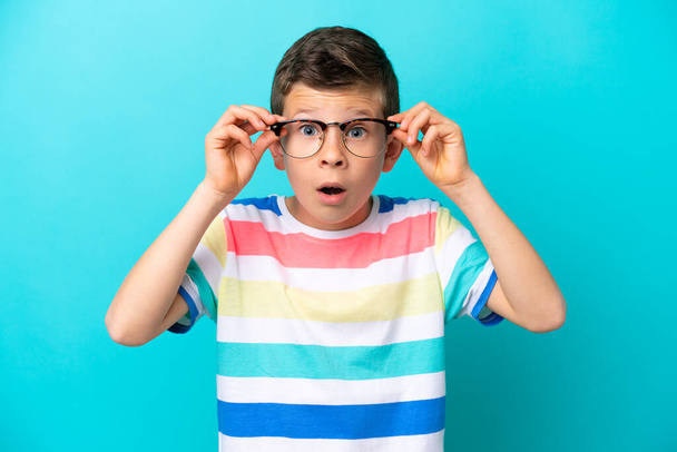Kleiner Junge isoliert auf blauem Hintergrund mit Brille und frustriertem Gesichtsausdruck - Foto, Bild