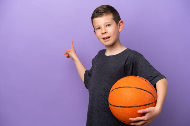 Kleiner Junge spielt Basketball isoliert auf lila Hintergrund zeigt zurück - Foto, Bild