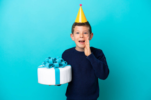 Kleiner Junge hält Geburtstagstorte isoliert auf blauem Hintergrund und schreit mit weit geöffnetem Mund - Foto, Bild