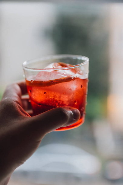 cheers with Campari, gin, vermouth cocktail with large ice and orange twist against window - Fotoğraf, Görsel