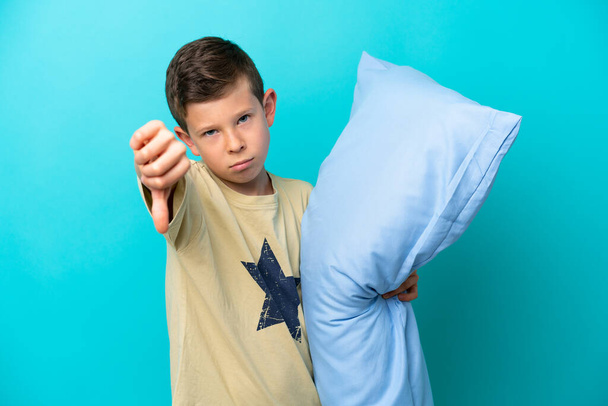 Menino de pijama isolado em fundo azul mostrando polegar para baixo com expressão negativa - Foto, Imagem