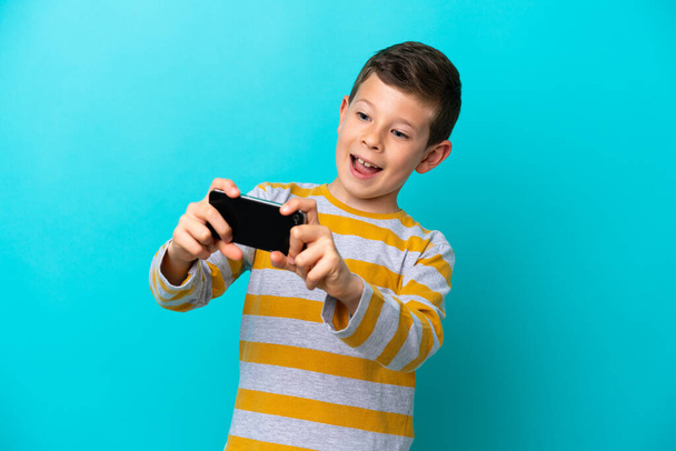 携帯電話で遊んでいる青い背景に隔離された小さな男の子 - 写真・画像