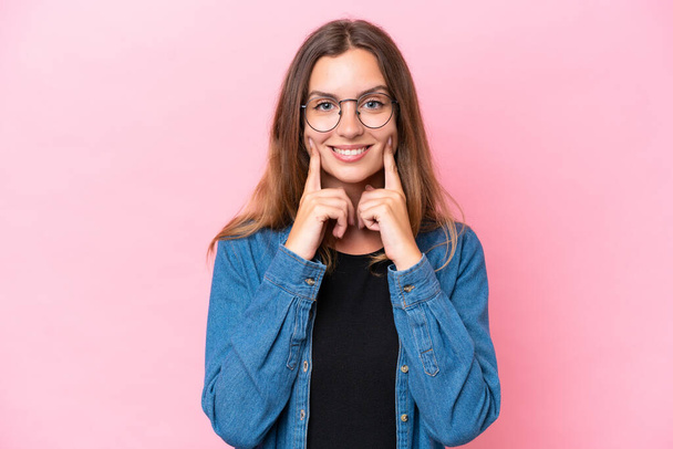Young caucasian woman isolated on pink background smiling with a happy and pleasant expression - 写真・画像