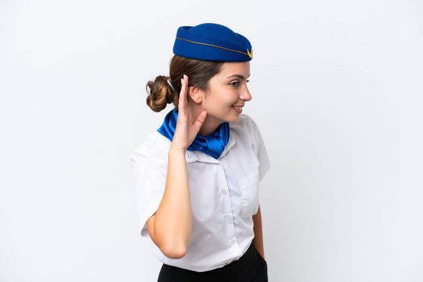 Airplane stewardess caucasian woman isolated on white background listening to something by putting hand on the ear - Foto, immagini
