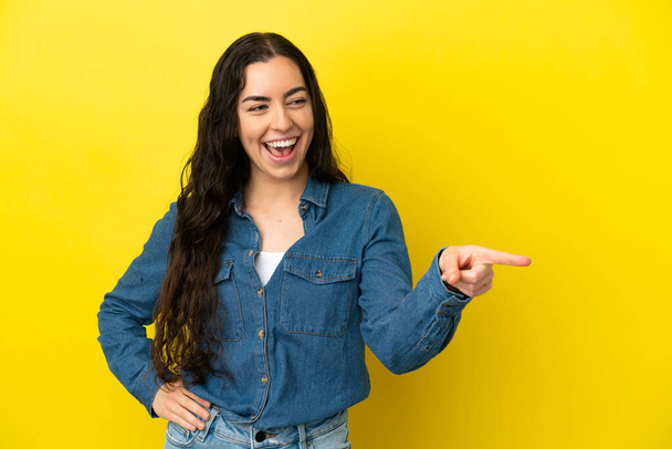 Young caucasian woman isolated on yellow background pointing finger to the side and presenting a product - Photo, Image