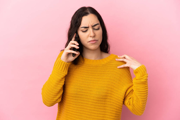 Young caucasian woman using mobile phone isolated on pink background suffering from pain in shoulder for having made an effort - Foto, imagen