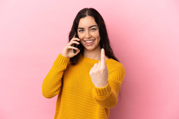 Young caucasian woman using mobile phone isolated on pink background doing coming gesture - Photo, image