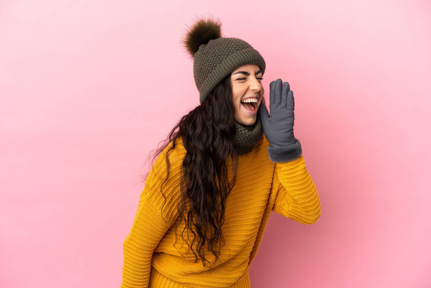 Young caucasian girl with winter hat isolated on purple background shouting with mouth wide open to the side - Zdjęcie, obraz