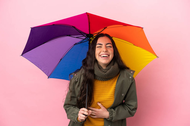 Mladá žena drží deštník izolované na růžovém pozadí s úsměvem hodně - Fotografie, Obrázek