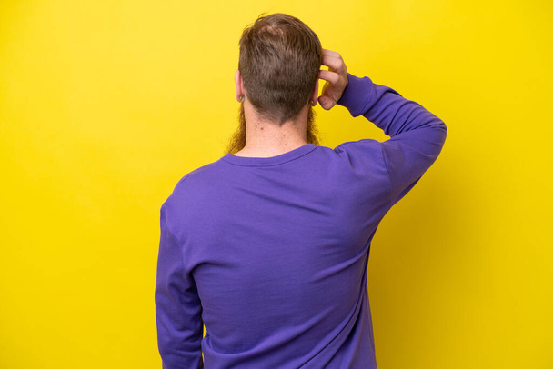 Rotschopf mit Bart isoliert auf gelbem Hintergrund in Rückenlage und Denken - Foto, Bild