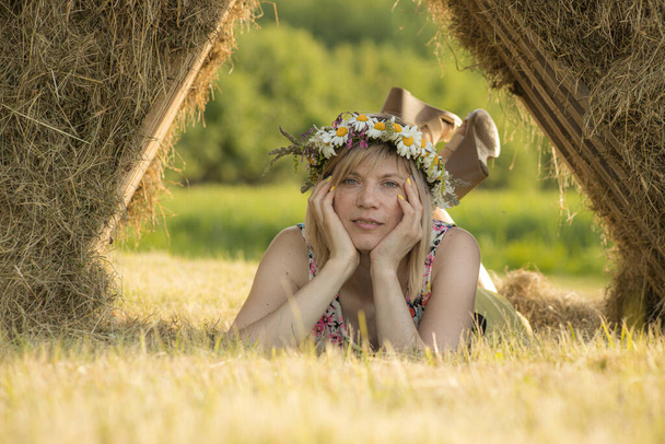 頭の上の花の花輪。冠を頭に被った女性。緑の中で真夏を祝う。オークのリースで真夏のお祝い - 写真・画像