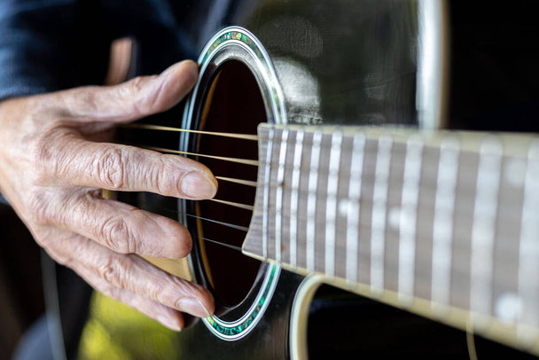 Elderly man right hand with amputated middle finger playing a black acoustic guitar - Fotoğraf, Görsel