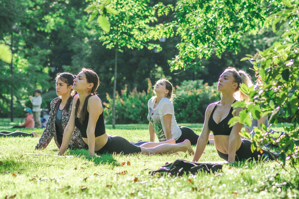 Vilnius, Lituania - 22 de junio de 2022: Hermosas chicas haciendo actividades al aire libre o al aire libre, yoga o gimnasio en el césped en un parque público en verano - Foto, Imagen