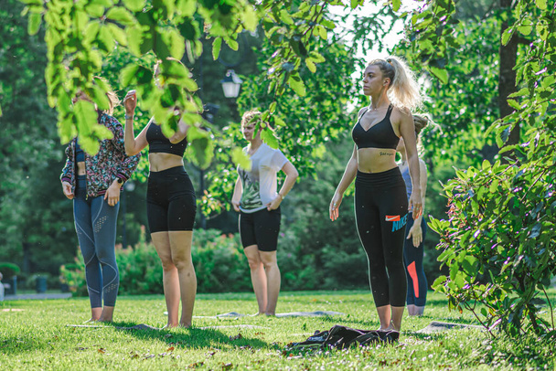 Vilnius, Litouwen - 22 juni 2022: Mooie meisjes die buiten- of buitenactiviteiten, yoga of gym op het gras maken in een openbaar park in de zomer - Foto, afbeelding
