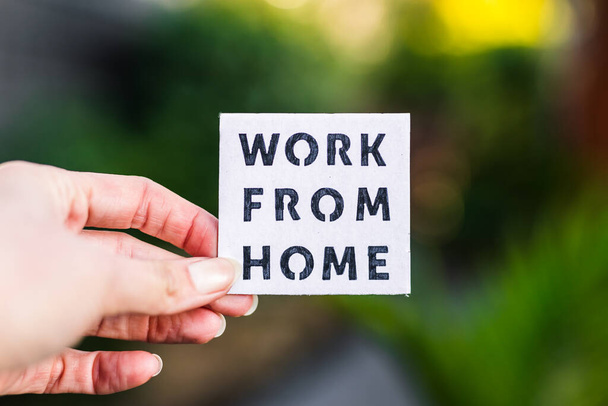 work from home sign being hold in front of out of focus lush green backard, concept of digital nomads working remotely or wfh days during lockdowns or covid-19 isolation - Foto, afbeelding