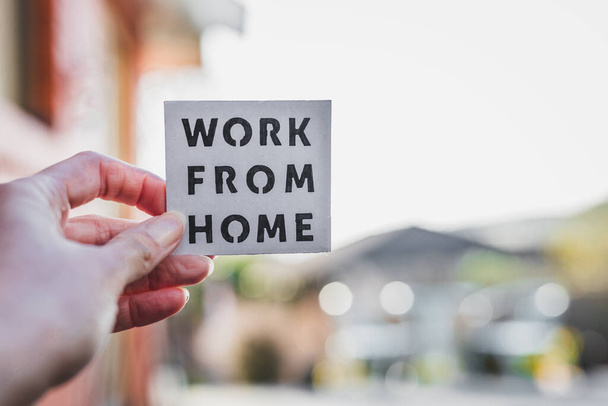 work from home sign being hold in front of out of focus backyard with table and chairs and home exterior, concept of digital nomads working remotely or wfh days during lockdowns or covid-19 isolation - Foto, immagini