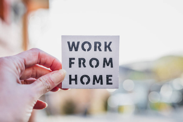 work from home sign being hold in front of out of focus backyard with table and chairs and home exterior, concept of digital nomads working remotely or wfh days during lockdowns or covid-19 isolation - Foto, imagen
