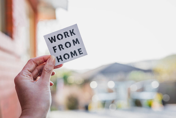 work from home sign being hold in front of out of focus backyard with table and chairs and home exterior, concept of digital nomads working remotely or wfh days during lockdowns or covid-19 isolation - Foto, immagini