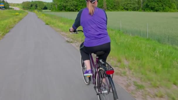 Вид женщины на велосипеде, передвигающейся по маленькой дороге на фоне живописного загородного пейзажа. Швеция.  - Кадры, видео