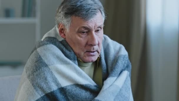 Sick caucasian man old grandfather suffering from fever elderly male at home wrapped warm blanket wipes sweat from forehead with napkin feels cold feeling unwell symptoms of coronavirus elderly covid - Footage, Video