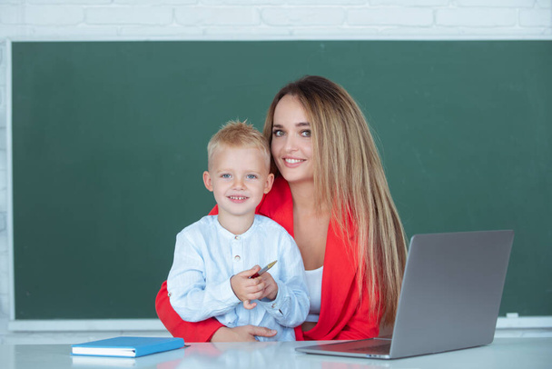 Elementary school teacher and pupil in classroom. Mother and son together using computer laptop - Foto, immagini