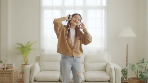 Młoda Azjatka w słuchawkach i tańcząca na podłodze w salonie. Szczęśliwa azjatycka kobieta uśmiech relaks w domu, zdrowe zdrowie psychiczne i samopoczucie - Materiał filmowy, wideo