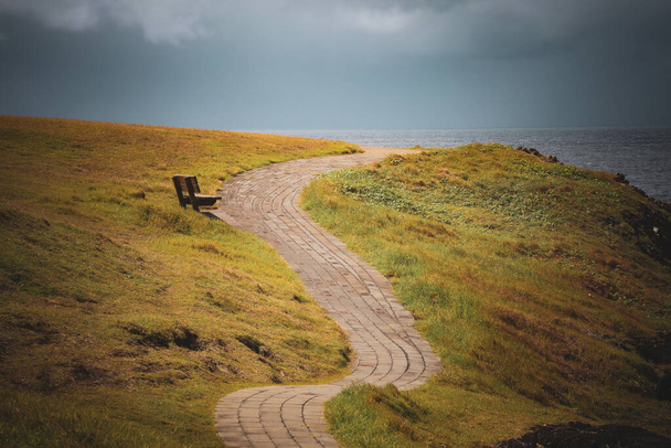 A stone walking path with two sides surrounded by lawn in the background of a seascape. - Фото, изображение