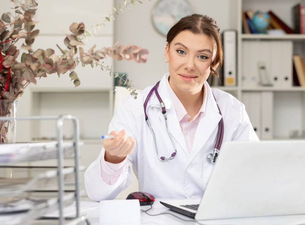 Portrait of female doctor who is working with laptop and documents in clinic - 写真・画像