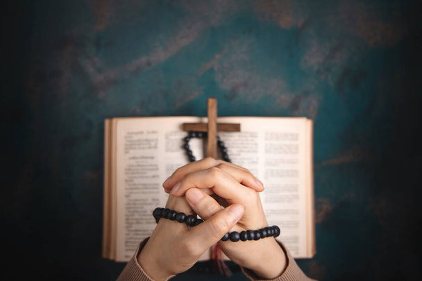 Spiritualiteit, Religie en Hoop Concept. Persoon die bidt door de Bijbel en kruis op het bureau. Symbool van nederigheid, smeekbede, geloof en geloof voor het Christelijke volk. Bovenaanzicht - Foto, afbeelding
