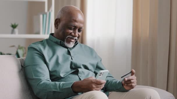 Afrikai öreg kopasz szakállas idősebb idős üzletember ideges nyugdíjas férfi van pénzügyi probléma az online átutalás fizetési hiba blokkolta a bankszámla probléma e-fizetés telefon app és hitelkártya - Felvétel, videó