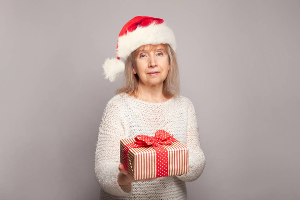 Noel 'i ve yeni yılı kutlamaya hazır mutlu, orta yaşlı bir kadının stüdyo portresi, Xmas hediye kutusu ve pozu. - Fotoğraf, Görsel