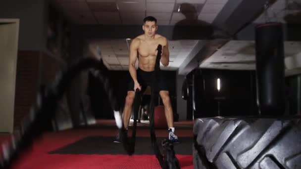 Fitness eğitimi - formda olmayan bir adam halatlara vurarak çapraz egzersiz yapıyor. Orta çekim - Video, Çekim
