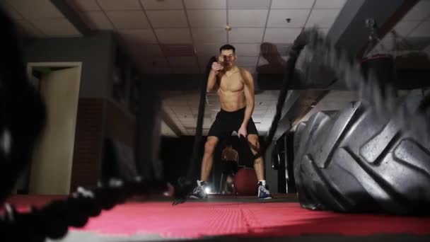 Fitnesstraining - fitter junger Mann ohne Hemd, der Crossfit-Übungen mit Seilschlagen macht. Mittelschuss - Filmmaterial, Video