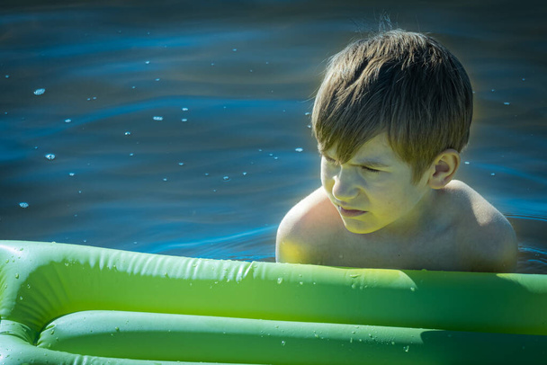 Le garçon dort sur un matelas gonflable dans l'eau. L'enfant seul dans l'eau. Un jeune homme sourit en dormant dans l'eau. Concentration sélective douce - Photo, image