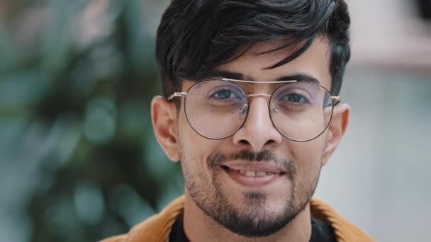 Férfi portré fejlövés fiatal jóképű boldog indiai srác nézi kamera mosolygós fogas mosoly sikeres magabiztos szakállas férfi modell pózol stílusos hipster okos diák szemüveges beltéri - Felvétel, videó