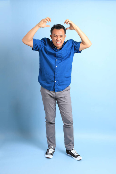 L'uomo asiatico di mezza età con camicia blu in piedi sullo sfondo blu. - Foto, immagini