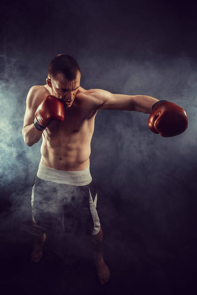Muscular kickbox or muay thai fighter punching in smoke.  - Photo, image