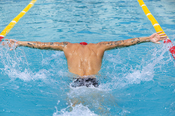 Perhosuintitekniikka. Nuori lihaksikas mies. Ammattimainen uimari suojalaseissa. Harjoittelua uima-altaalla, ulkona. Urheilu, voima, energia, tyyli, harrastus käsite. Taivaallinen sininen vesi - Valokuva, kuva