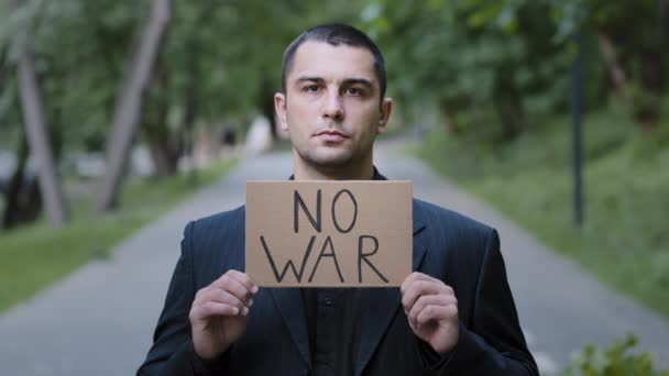 Serious strong caucasian adult man activist standing outdoors demonstrating cardboard plate with words no war protesting against the Russian invasion banner antiwar inscription message ask for support - Footage, Video